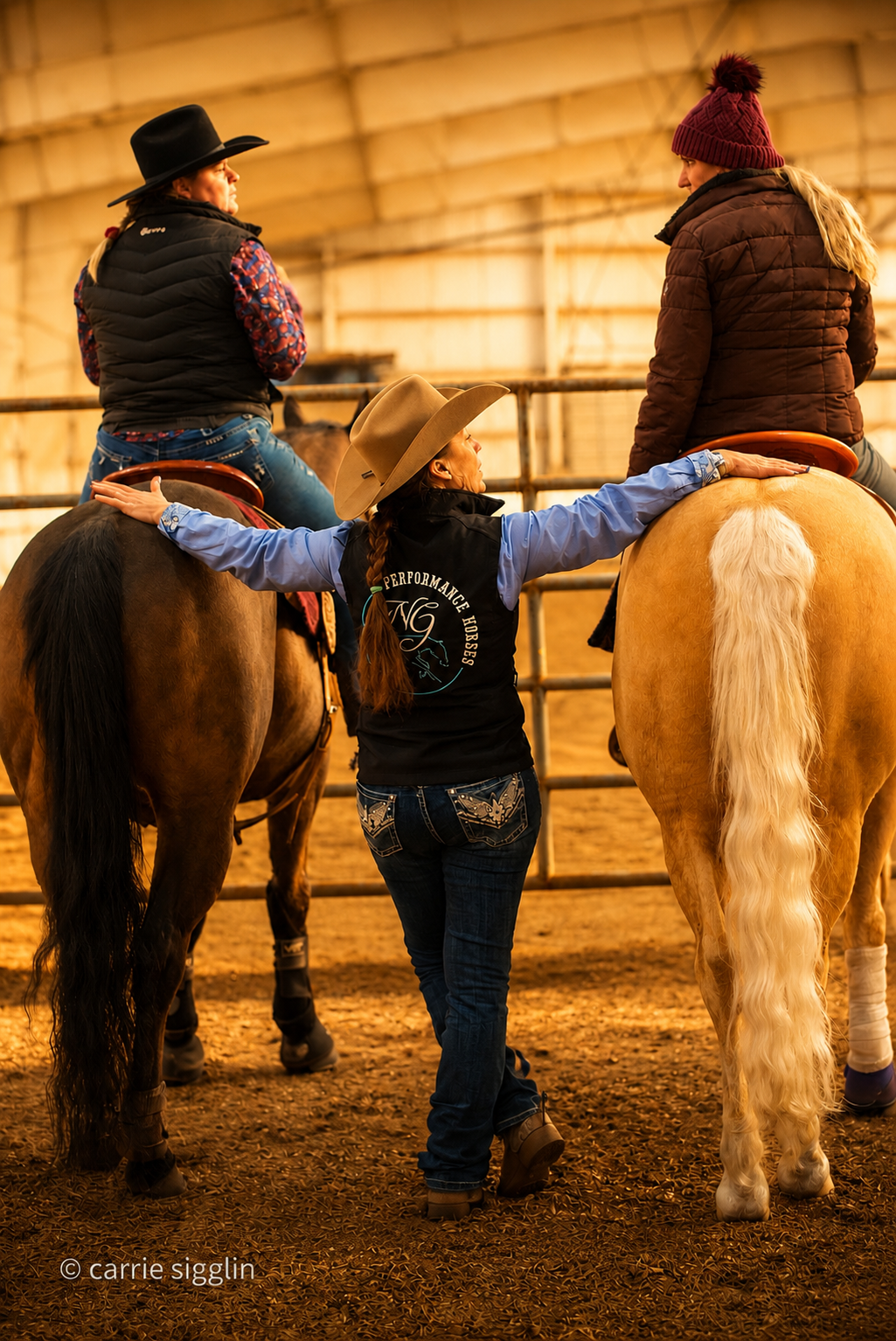 Peggy coaching two riders on horseback in the arena, arms outstretched toward both horses