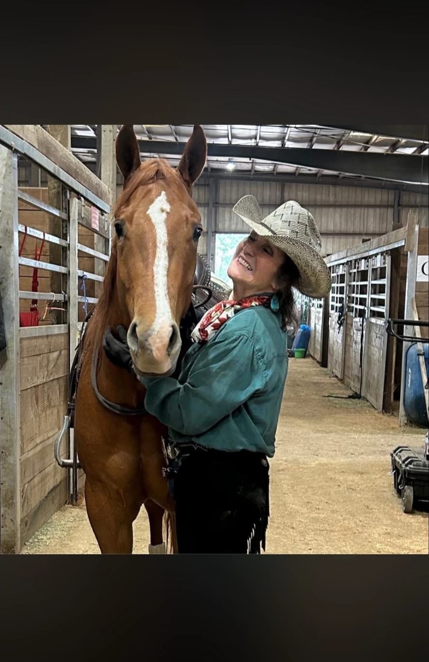 Donna Pinkerton Kamstra smiling beside her sorrel horse in a barn aisle