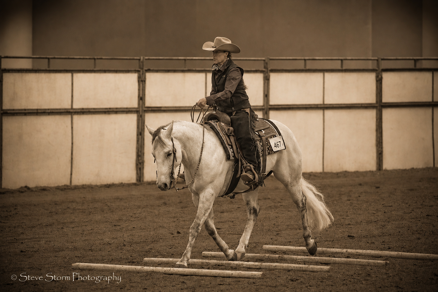 Rider on a white horse walking over ground poles in an indoor arena