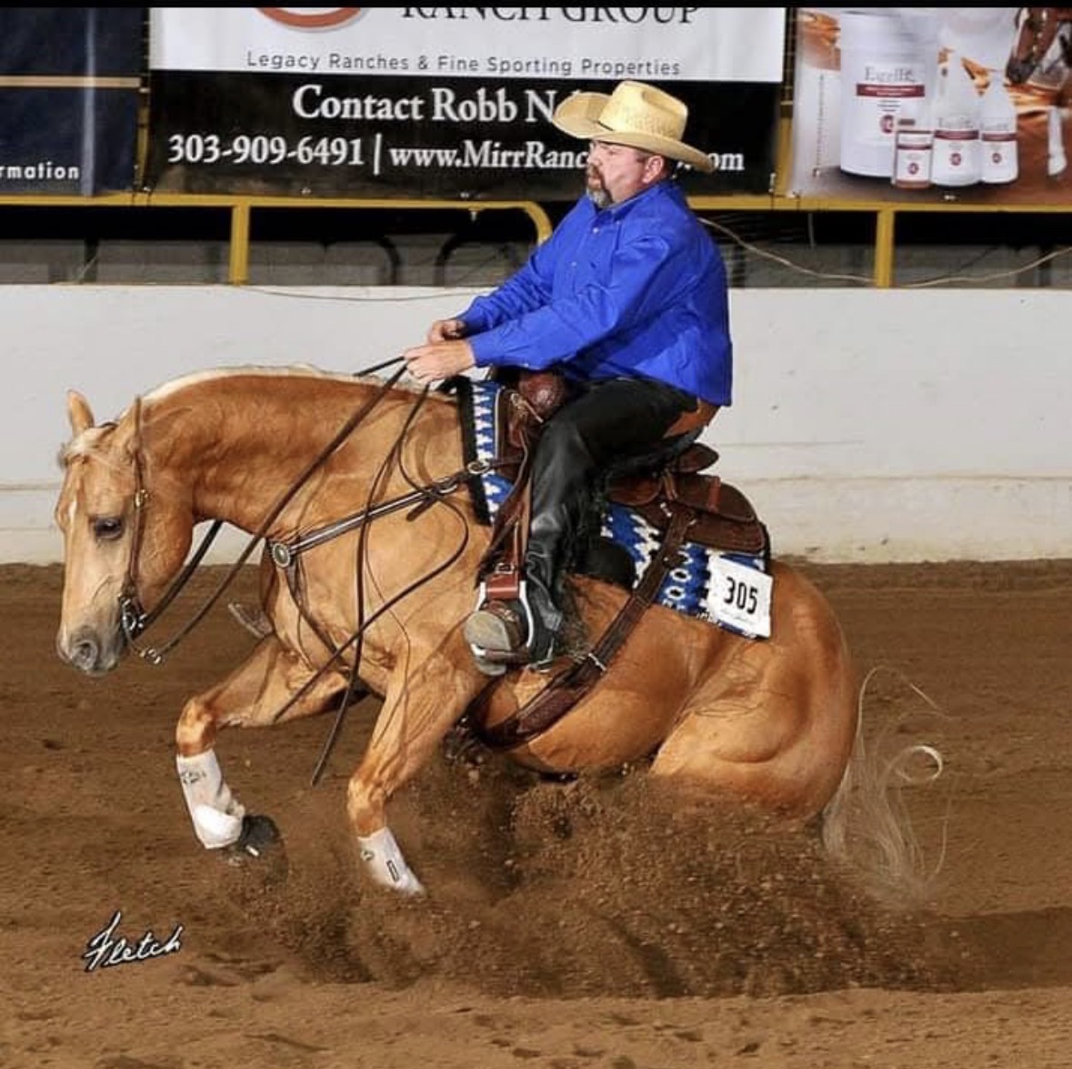 Reining horse sliding to a stop in a show arena, ridden by a trainer in a blue shirt